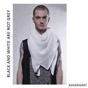 Male model with short hair and beard looking into the camera. Wearing a white scarf out of lightly woven material with white outlines and a black tank top. Both upper arms got tattoos. in the background is a white wall. font left side from down to up: black and white are not grey. font right down corner: kaigerhardt