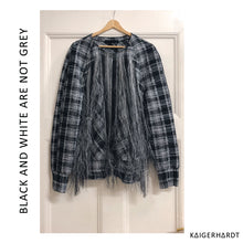 Front view. Checkered black and white sweater withe fringes and raglan sleeves on a hanger hanging on a door. font left side from down to up: black and white are not grey. font right down corner: kaigerhardt