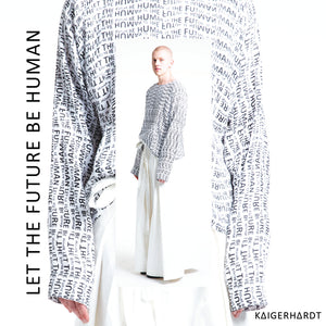 Paulius is wearing a white light sweater which has an all over print in small letters which says let the future be human. The sweater has long sleeves so that you only see the finger tips of the model. withe the sweater he wears a white long wide pair of trousers in hakama style made out of denim. 