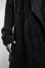 Detail. A black draped cardigan in unregular grid optic with a crossing front. The cardigan is made in Berlin Germany    Colour: black Material: overgarment 100% PE                lining               80% wool, 20% cotton