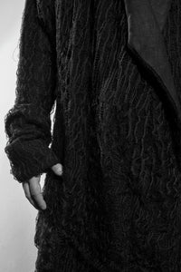 Detail. A black draped cardigan in unregular grid optic with a crossing front. The cardigan is made in Berlin Germany    Colour: black Material: overgarment 100% PE                lining               80% wool, 20% cotton
