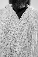 Detailshoot. A white draped cardigan in unregular grid optic with a crossing front. The cardigan is made in Berlin Germany    Colour: overgarment: white              lining: black, white Material: overgarment 100% cotton                lining               80% wool, 20% linen 