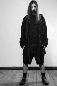 Front. A black draped cardigan in unregular grid optic with a crossing front. The cardigan is made in Berlin Germany    Colour: black Material: overgarment 100% PE                lining               80% wool, 20% cotton